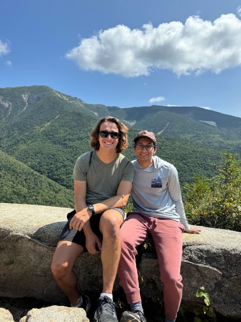 Thinkstruct co-founders sitting together on a rocky overlook with mountains behind them.